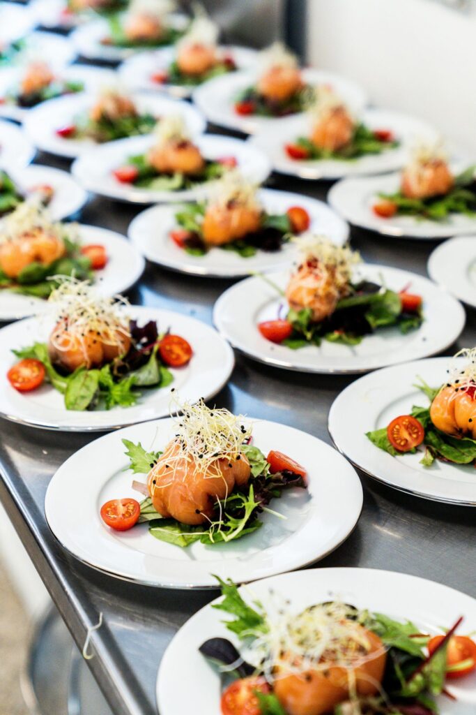 Platos de catering gourmet emplatados con salmón y ensalada en cocina profesional en Valencia
